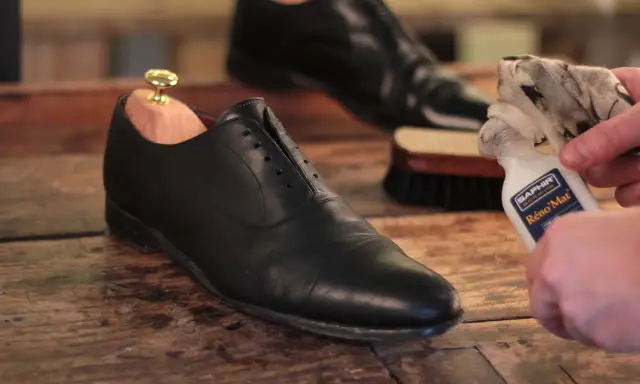 Schuhe polieren: Ein schwarzer Lederschuh mit Schuhspanner wird mit einem Tuch und Saphir Reno'Mat gereinigt.