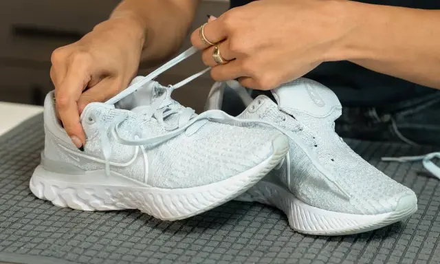 Hände binden hellblaue Nike Schuhe, bereit für die Waschmaschine.