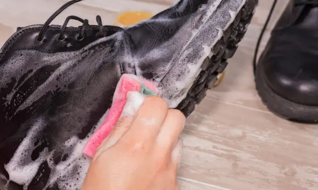 Schwarze Lederschuhe werden mit einem Schwamm und Seifenschaum gereinigt. Die Sohle und das Leder werden sorgfältig abgerieben, um sie wieder sauber zu machen.