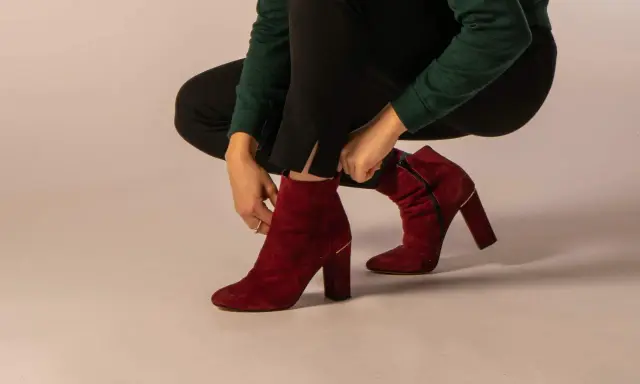 Eine Frau zieht rote Wildleder-Stiefeletten an. Verschiedene lederarten schuhe sind hier zu sehen, wie diese eleganten Damenschuhe.