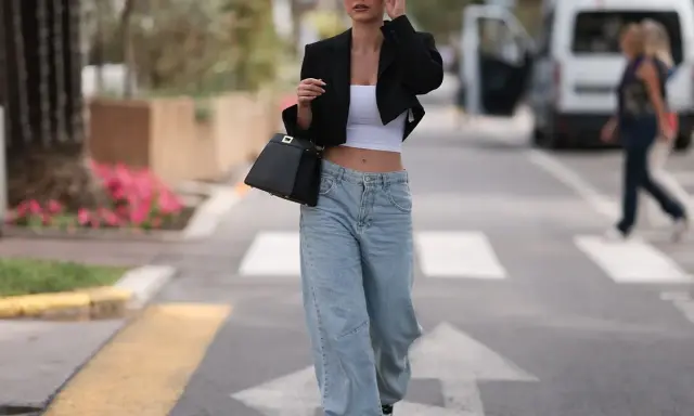 Frau in einem lässigen Baggy Jeans Outfit mit schwarzem Blazer und weißem Crop-Top, unterwegs in der Stadt.