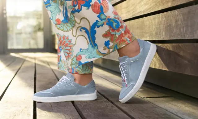 Blaue Wildlederschuhe mit weißer Sohle und dezenter Ziernaht am Schuh, kombiniert mit einer Hose mit floralem Muster.