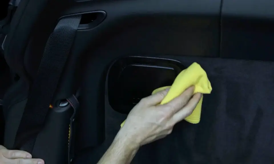 Hand wischt mit gelbem Tuch über schwarzes Kunstleder im Auto. So einfach ist Kunstleder reinigen.