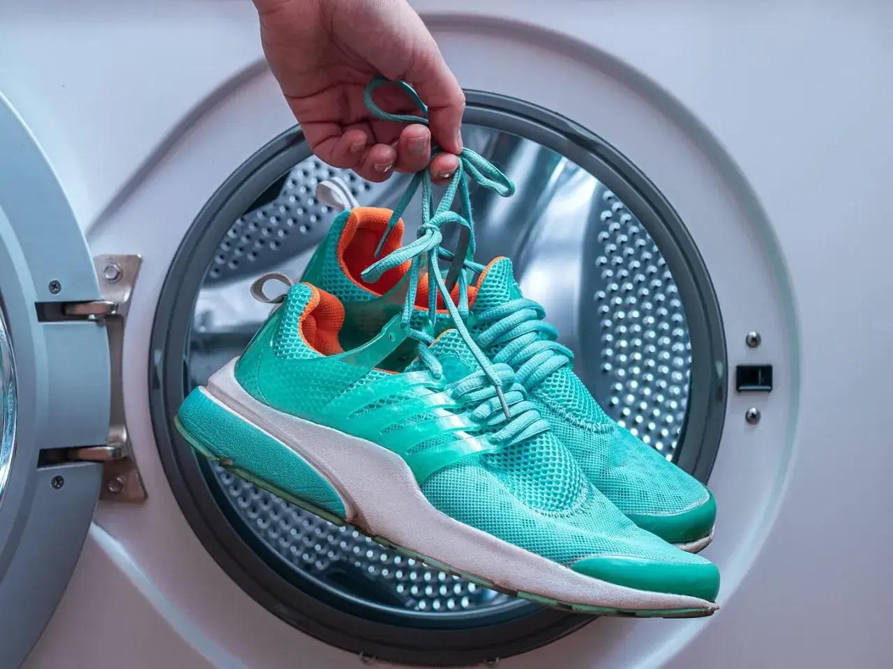 Skechers waschen wieviel Grad? Türkise Turnschuhe werden vor dem Waschen in der Waschmaschine gehalten.