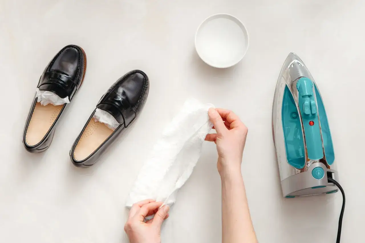 Schwarze Lederschuhe werden mit einem feuchten Tuch und einem B&uuml;geleisen behandelt, um Falten aus lederschuhen zu entfernen.