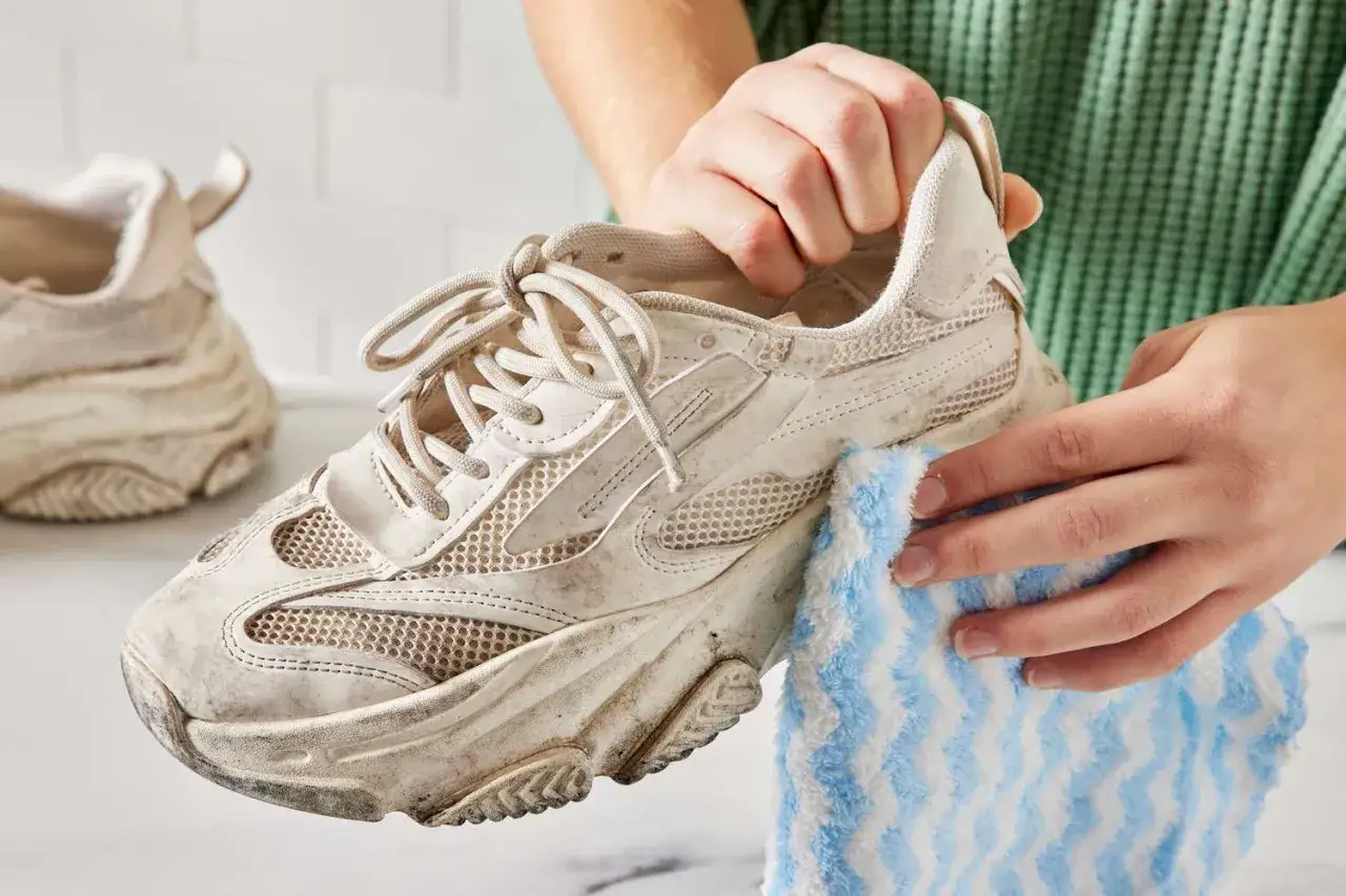 Schmutzige Puma Schuhe werden mit einem blau-weißen Tuch gereinigt.