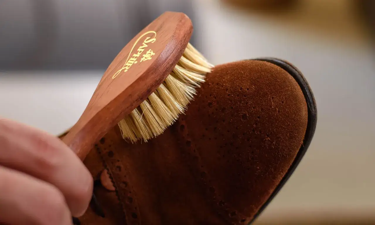 Bürste mit Holzgriff reinigt braunen Wildlederschuh. Perfekt für die Fettleder Pflege.