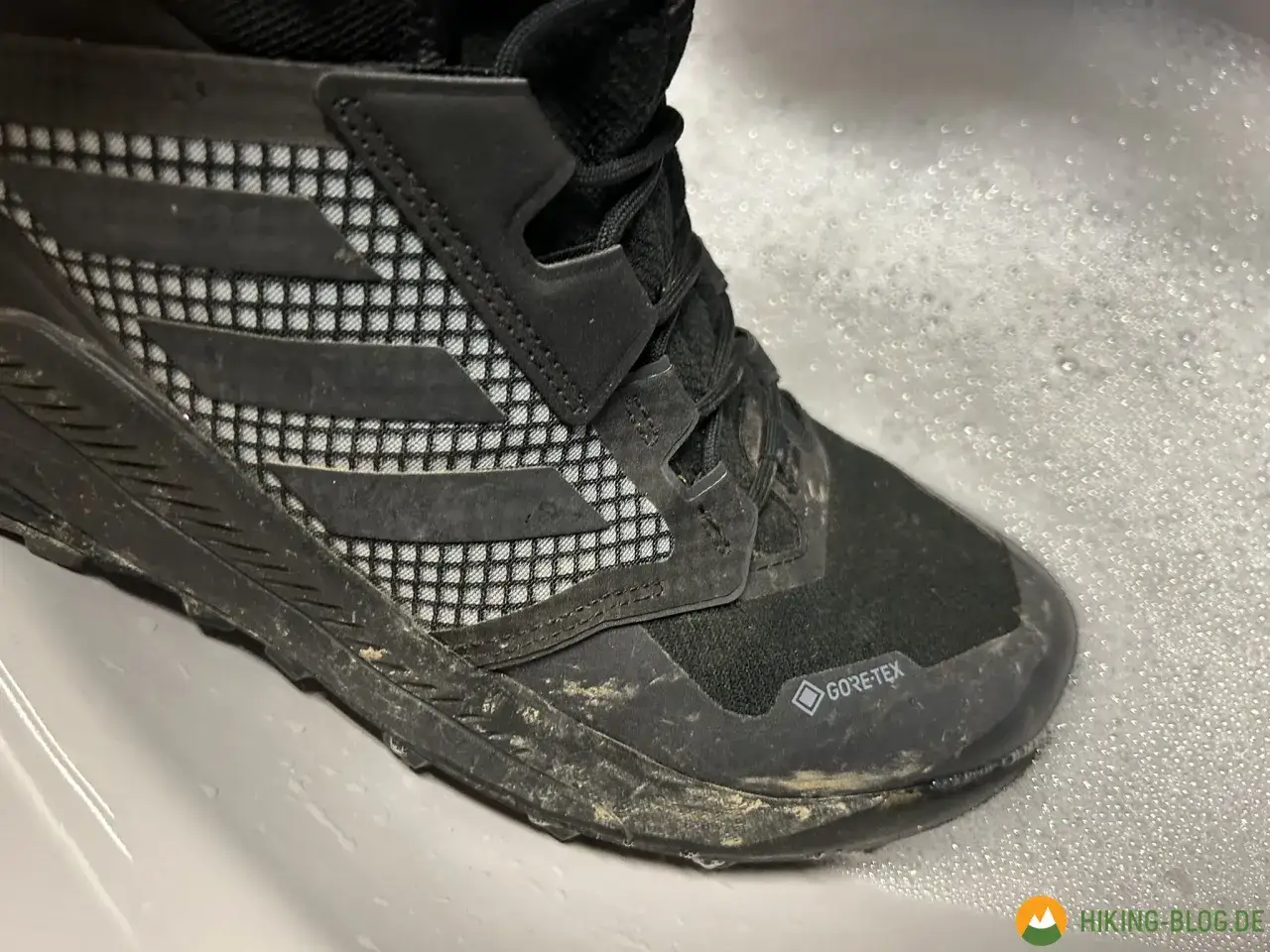 Schmutziger adidas Terrex Schuh im Schaumbad, bereit f&uuml;r die Waschmaschine.