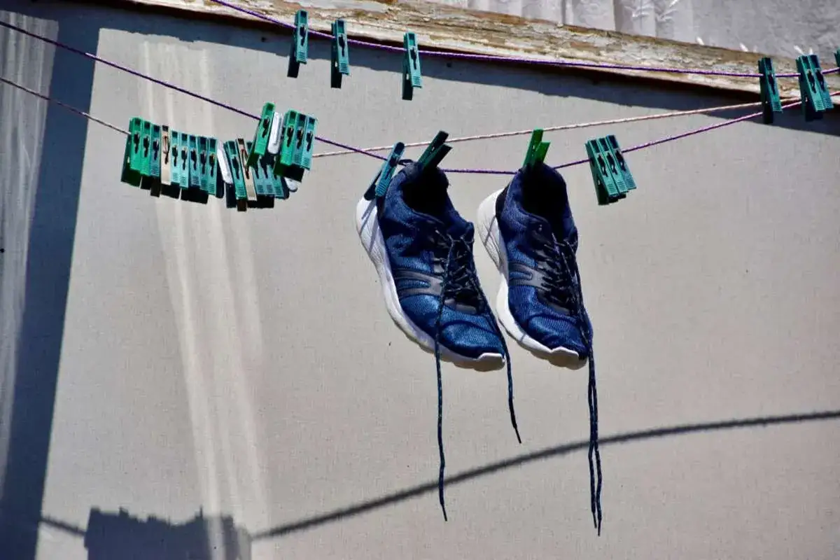 Blaue Turnschuhe trocknen an einer Wäscheleine, befestigt mit grünen Klammern.