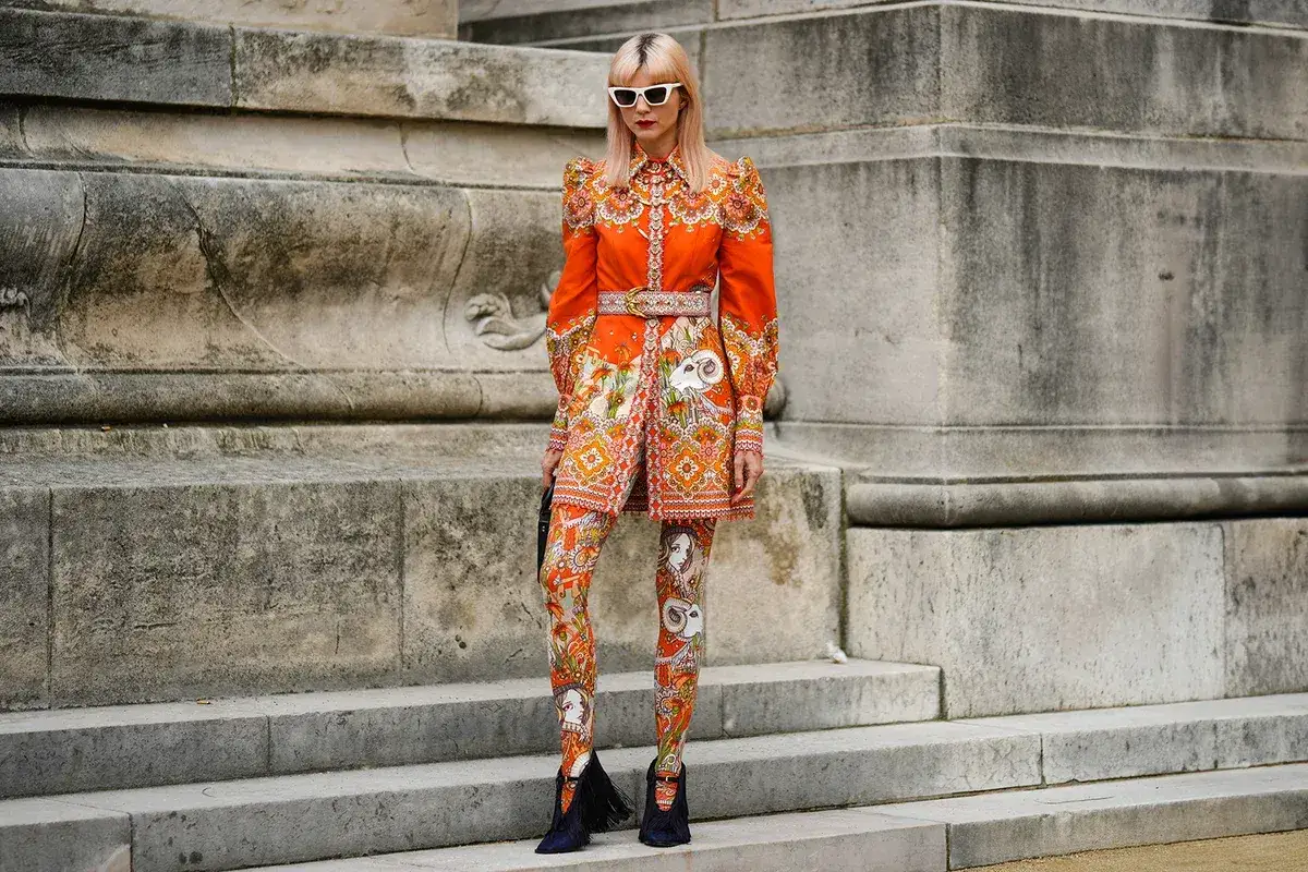 Frau in einem auffälligen orangefarbenen Kleid mit passenden Leggings, das mit einem detailreichen Muster verziert ist.