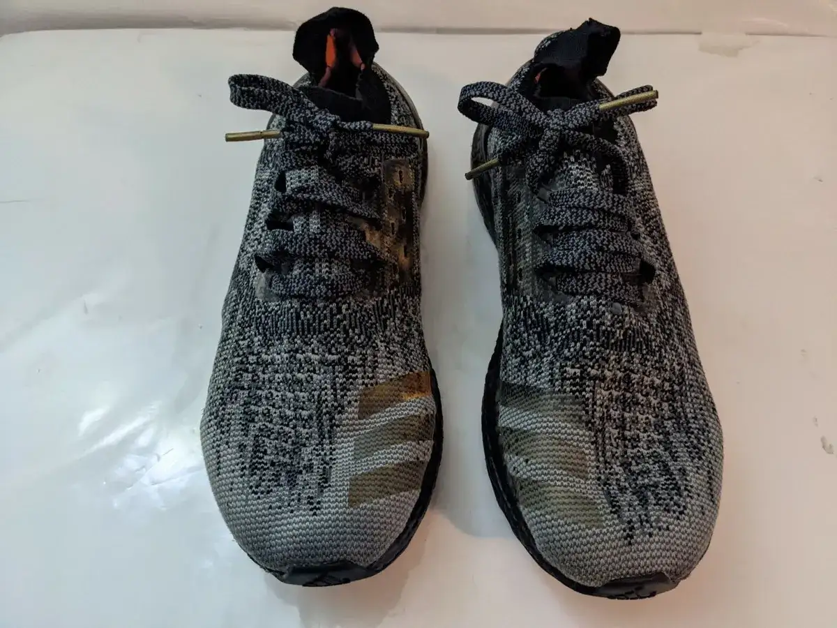 Zwei graue Adidas BB3900 Laufschuhe mit Camouflage-Muster und goldenen Streifen.