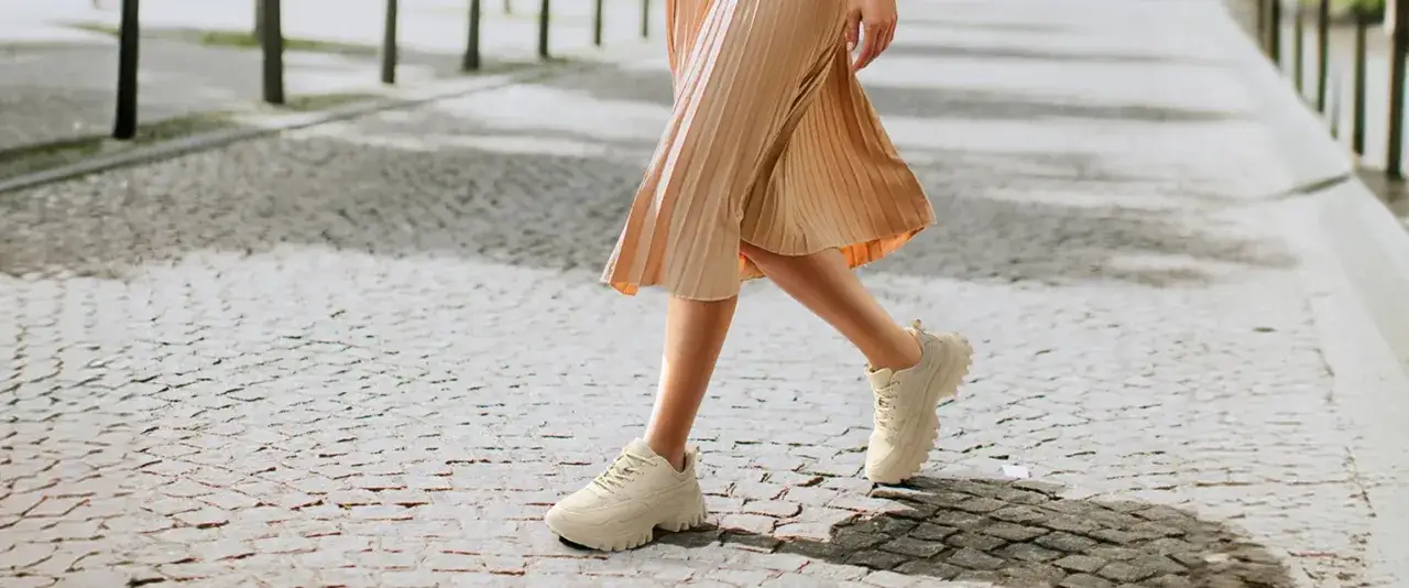 Beige Sneaker kombinieren: Ein luftiger Faltenrock trifft auf klobige, cremefarbene Sneaker. Ein l&auml;ssiger Look f&uuml;r unterwegs.