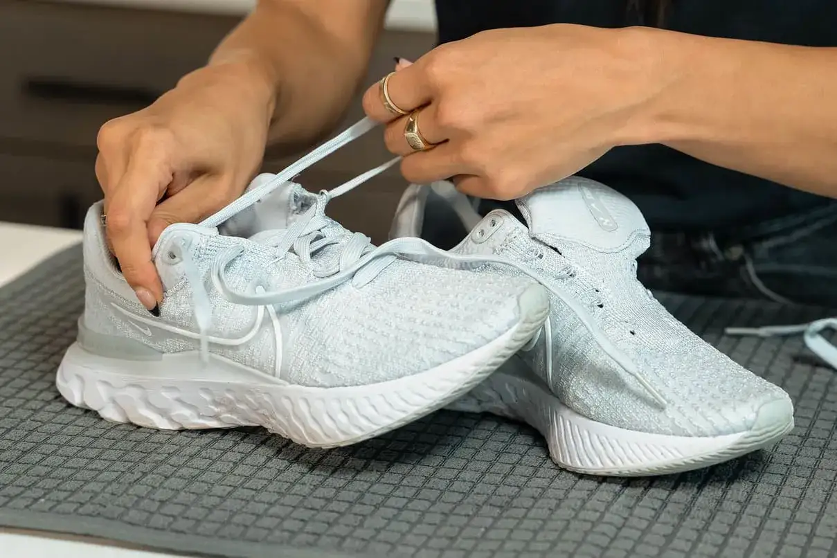 H&auml;nde binden hellblaue Nike Schuhe, bereit f&uuml;r die Waschmaschine.
