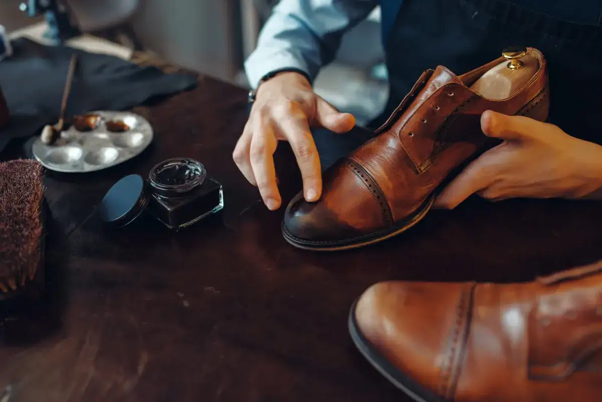 Hände polieren braune Lederschuhe mit schwarzer Schuhcreme. Ein Schuhspanner ist im Schuh.