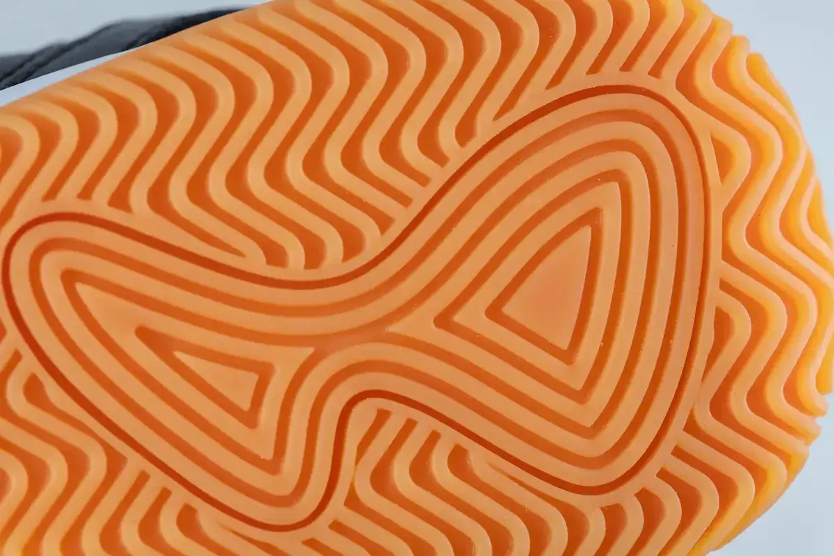 Nahaufnahme einer leuchtend orangen Schuhsohle aus Gummi oder Kunststoff mit einem wellenf&ouml;rmigen Profil f&uuml;r optimalen Halt.
