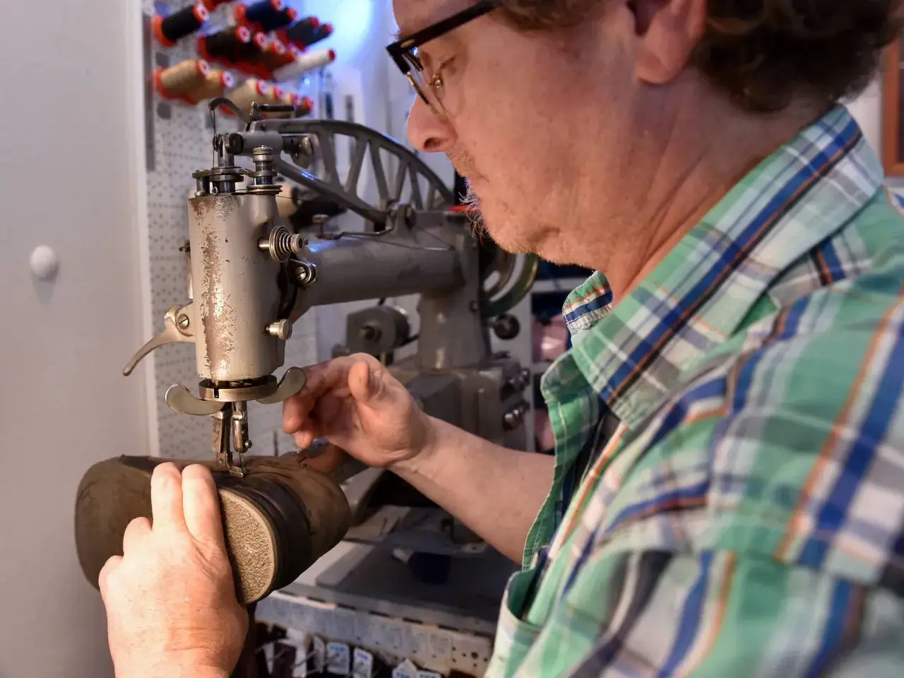 Ein Mann mit Brille arbeitet an einer Nähmaschine für Schuhe. Er ist ein Schuster, der alte Schuhe repariert.