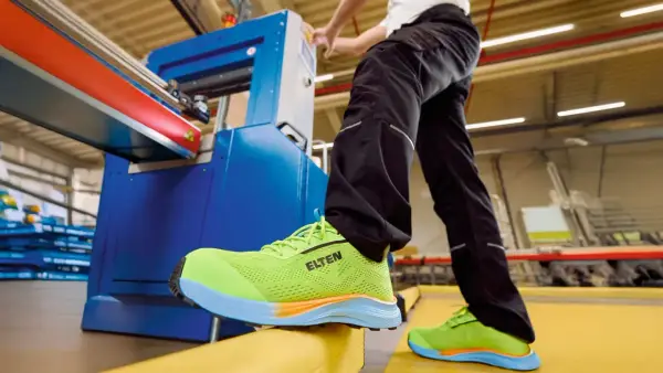 Arbeiter in leuchtend grünen Sicherheitsschuhen von ELTEN an einer Maschine. Seit wann gibt es Schuhe? Schon seit der Steinzeit, um die Füße zu schützen.